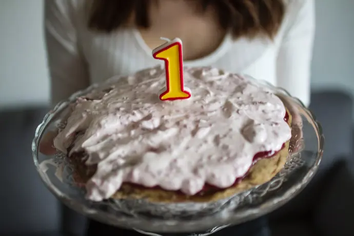 a woman holding a cake with a one candle on it