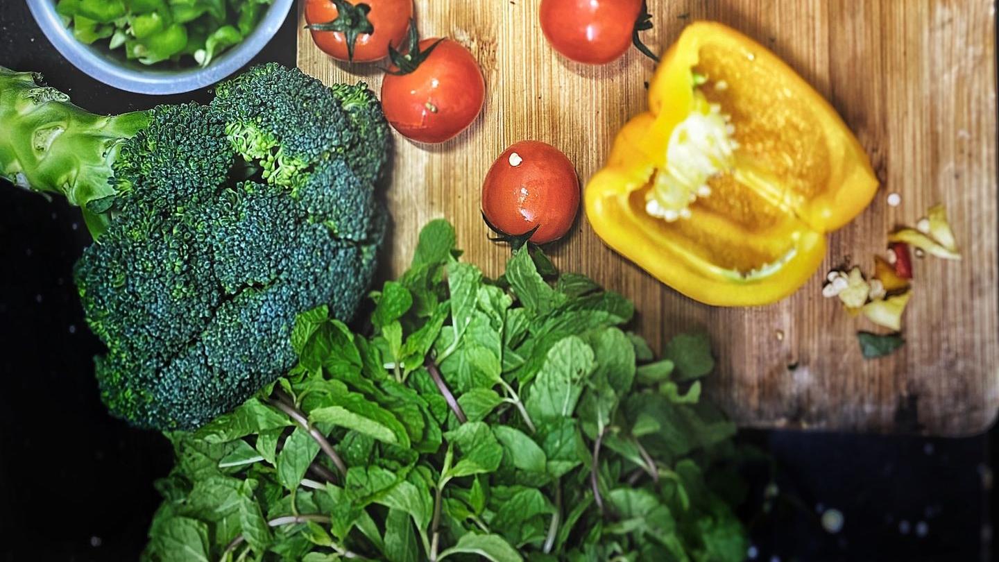 orange tomatoes near sliced yellow bell pepper, broccoli on wooden chopping board